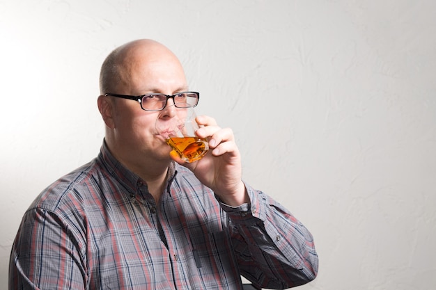 Foto anciano calvo con gafas bebiendo un vaso de brandy o whisky mirando hacia el lado con una expresión seria