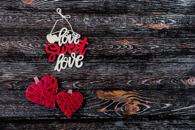 Foto aufschrift „love sweet love“ rote gewebte herzen der liebe auf dunklem holzhintergrund