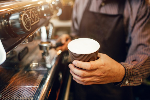 Foto barista in der schürze hält eine tasse kaffee mit schwimmender milch