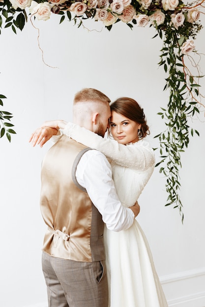 Braut und Bräutigam umarmen sich unter einem Blumenbogen