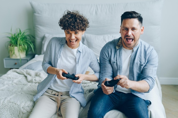Foto casal fofo namorado e namorada jogando videogame sentado na cama no quarto