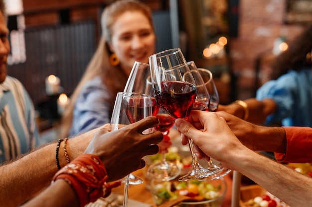 Cerca de jóvenes sosteniendo copas de vino y brindando mientras celebran juntos en la mesa durante