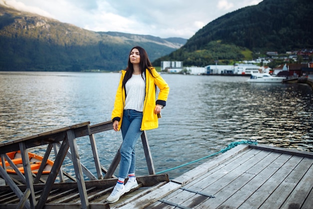 Chica turista en una chaqueta amarilla posando en el lago en Noruega Aventura de estilo de vida itinerante