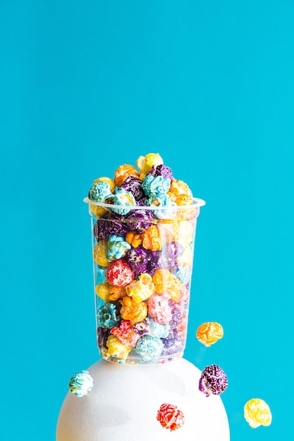 Foto composición creativa con palomitas de maíz de colores en un vaso transparente
