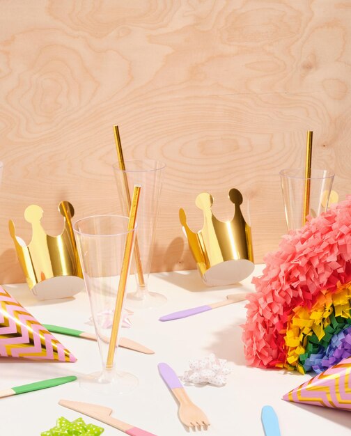 Foto concepto de fiesta de cumpleaños fiestas piñata cubiertos sombreros festivos vasos de plástico con pajitas y coronas de oro en mesa blanca
