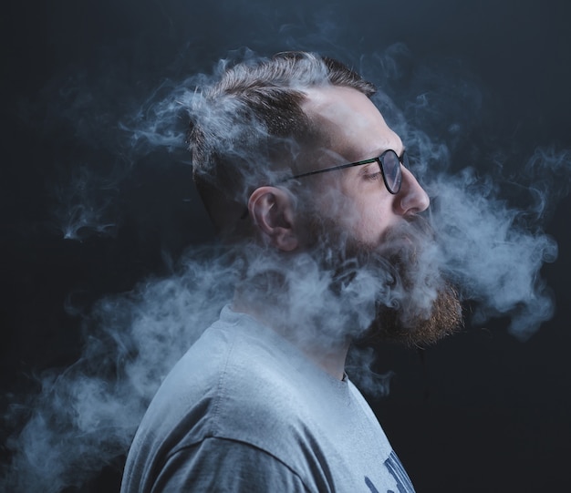 Concepto. El humo envolvió al hombre de la cabeza. Retrato de un hombre barbudo y elegante con humo.