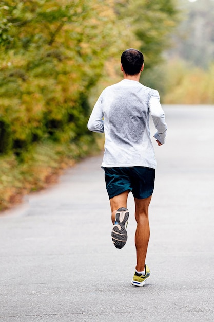 Foto corredor masculino corriendo en el parque de otoño con sudor en la espalda en la ropa