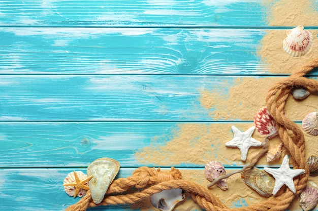 Foto cuerda del mar con muchas conchas marinas diferentes en la arena de mar en una vista superior de madera azul