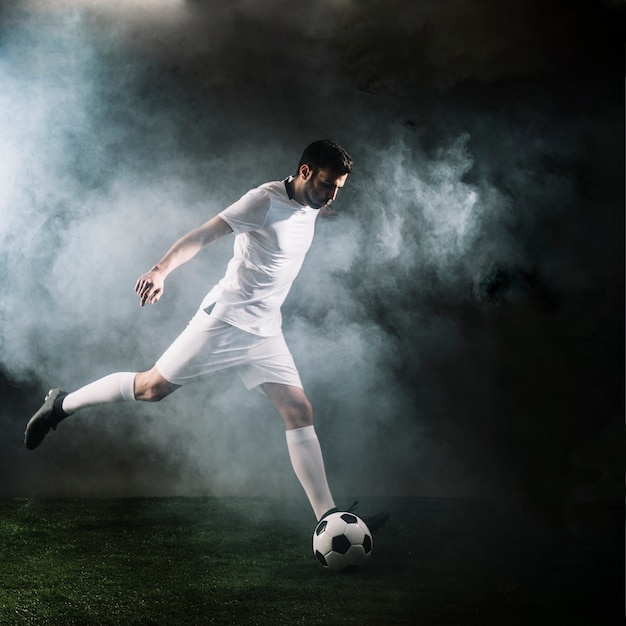 Deportista pateando el balón de fútbol en el humo