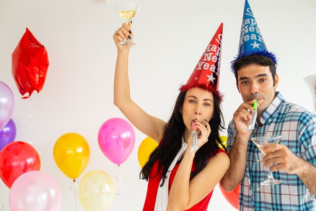 Foto dos silbatos de fiesta que soplan caucásicos frente a globos de colores fiesta de año nuevo 2020.