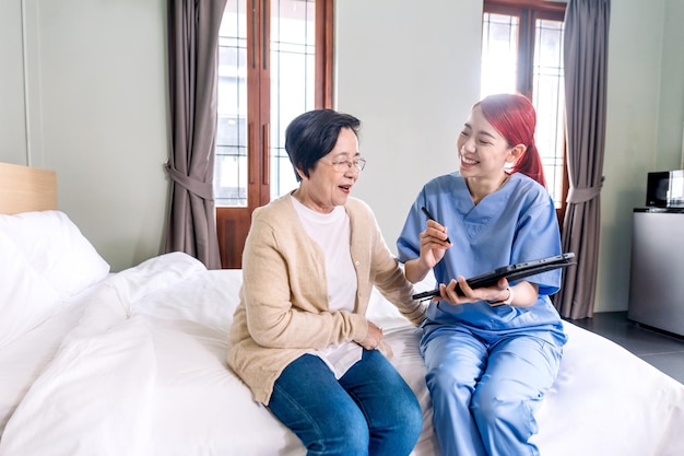 Enfermeira de terapia de mulher asiática vestindo jaleco relata o estado de saúde da mulher asiática sênior com tablet digital no quarto Visita do cuidador em casa Cuidados de saúde em casa e conceito de casa de repouso