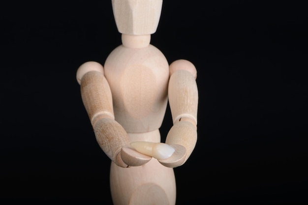Figura de madera humana sostiene en las manos un puente de zirconia con glazour sobre un fondo negro