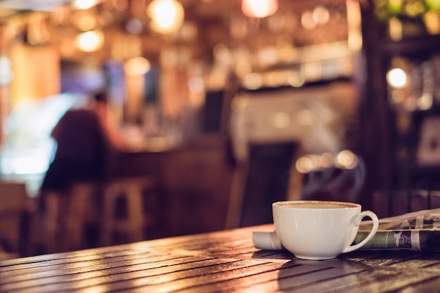 Foto heiße espressokaffeetasse mit zeitung auf dem holztisch, der bokeh unschärfehintergrund beleuchtet