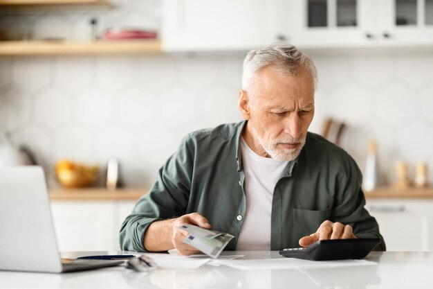 Foto hombre mayor concentrado con efectivo en la mano calculando las finanzas en casa