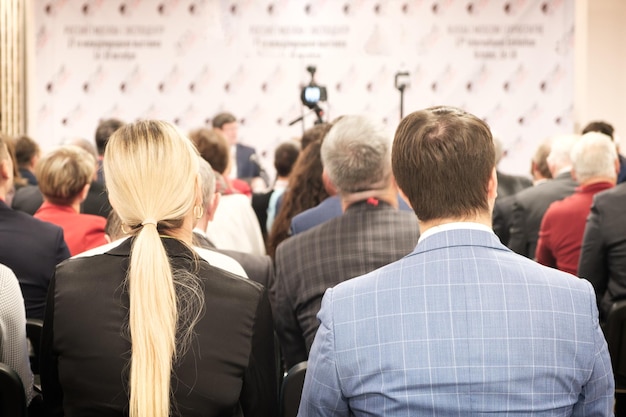 Foto hombre de negocios y mujer rubia con cabello largo y gente escuchando en la conferencia o en el entrenamiento en la sala
