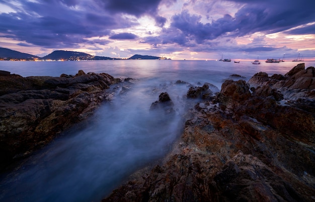 Imagen de larga exposición del paisaje marino dramático del cielo con la roca en paisaje de la puesta del sol