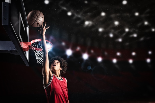Foto jogador de basquete com uniforme vermelho pulando alto para dar uma enterrada na cesta