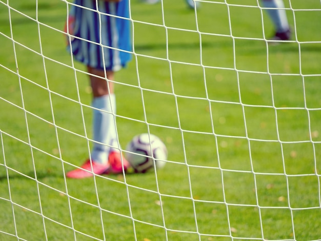 Foto joven portero de fútbol en el campo de fútbol fuera de enfoque a través de la red de la puerta de fútbol