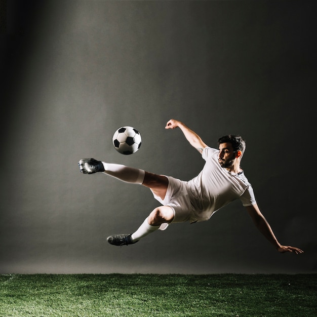 Jugador de fútbol barbudo cayendo y pateando la pelota