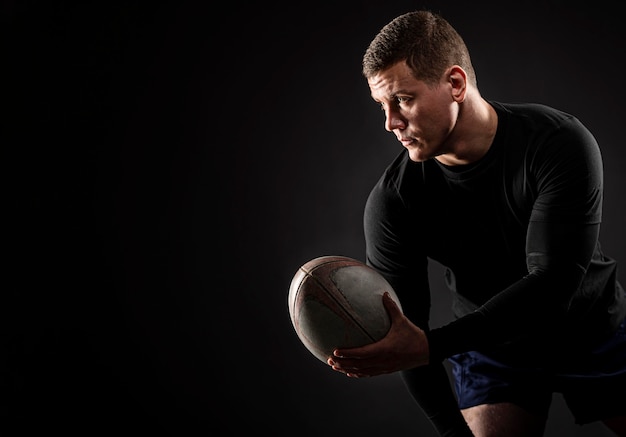 Jugador de rugby masculino guapo atlético sosteniendo la bola con espacio de copia