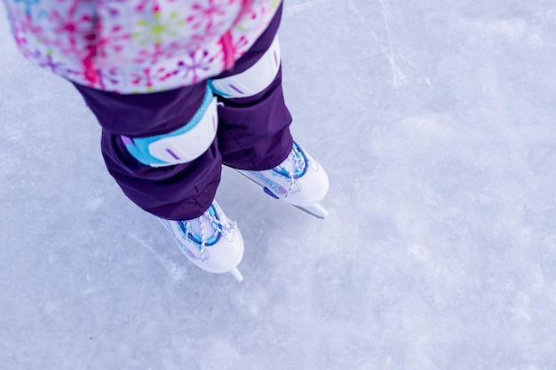 Foto kleines mädchen in winterkleidung mit schutz beim schlittschuhlaufen auf der eisbahn. erste lektion über eiswinteraktivitäten