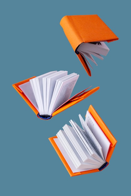 Foto libros en miniatura en una cubierta naranja vuelan sobre un fondo azul.