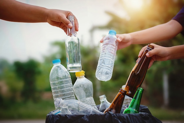 Foto mano de personas sosteniendo plástico y vidrio de botella de basura en bolsa de reciclaje para limpieza
