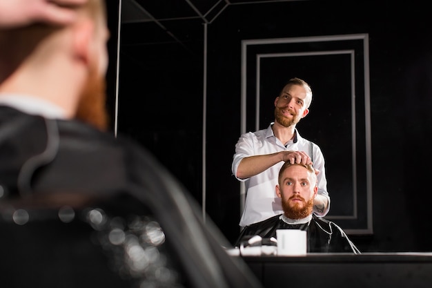 Foto el maestro corta el cabello y la barba en la peluquería. peluquero hace peinado con tijeras y peine de metal.