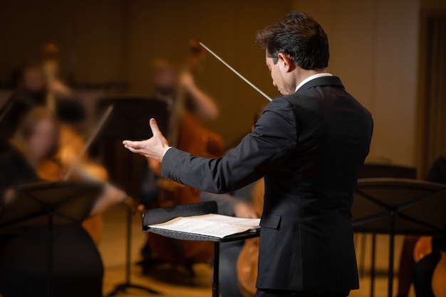 Foto maestro da orquestra sinfônica com intérpretes no fundo da sala de concertos