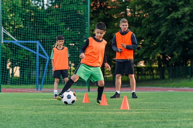 Muchacho adolescente en ropa deportiva entrena fútbol en campo de fútbol.