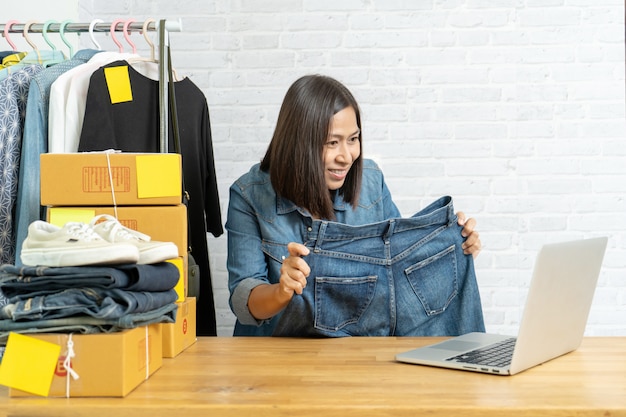 Foto mujer asiática que usa el teléfono móvil inteligente que toma la venta en vivo pantalones vaqueros en línea