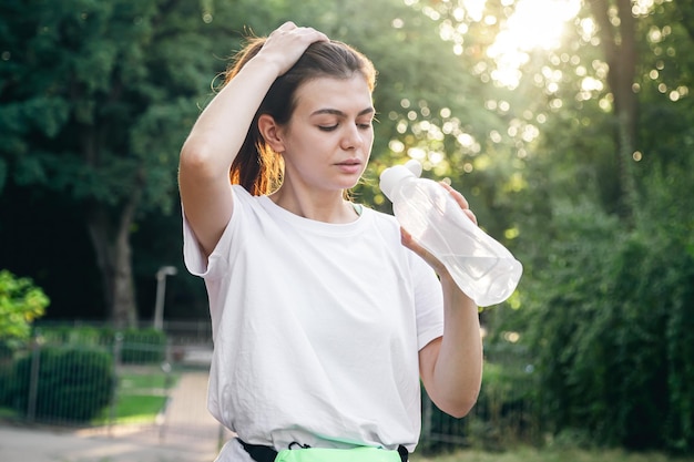 Foto mujer joven atractiva bebiendo agua después de hacer ejercicio al aire libre concepto de trote