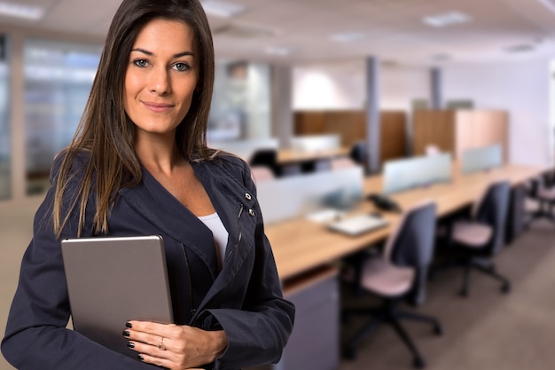 Mujer de negocios brasileña con tableta mirando a cámara en espacio de oficina borrosa. Copie el espacio.