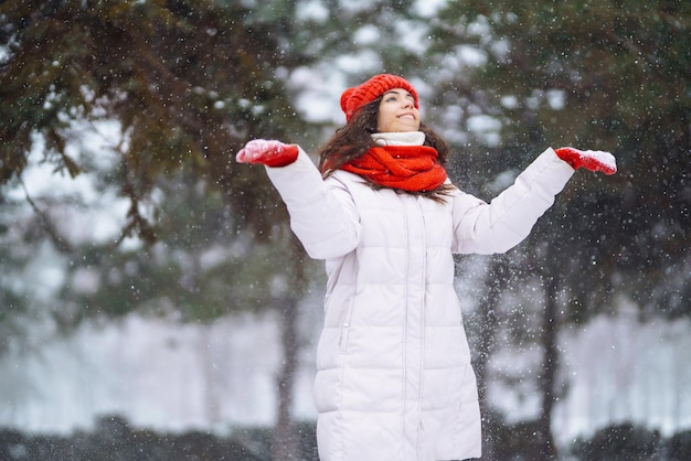 Mujer sonriente de invierno con sombrero rojo posando en un parque nevado Clima frío Vacaciones de moda de invierno