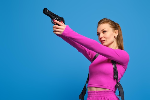 Mulher elegante em terninho de malha roxo aponta uma arma sobre o fundo azul do estúdio Polícia da moda e acerto preciso no conceito de alvo