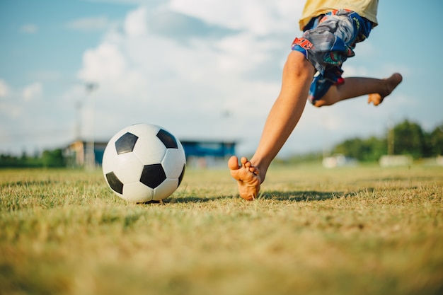 Foto niño pateando una pelota con el pie descalzo mientras jugaba fútbol