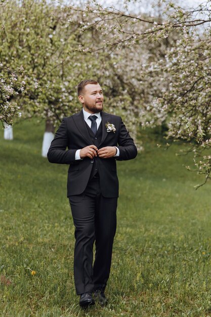 Foto o noivo vestido de fato preto caminha para a frente na grama verde na natureza um homem elegante em um traje preto clássico