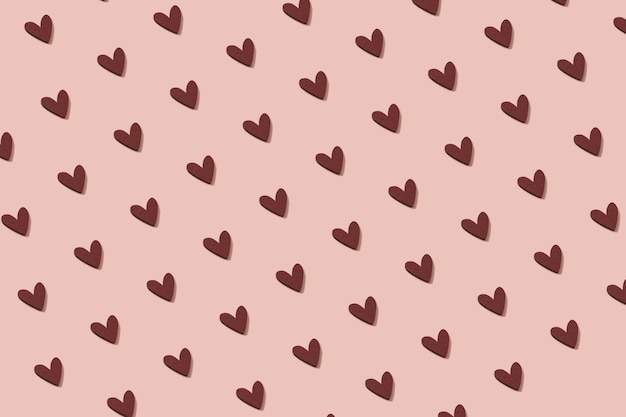 Foto patrón sin fisuras de adorno de corazón de madera sobre un fondo rosa pastel.