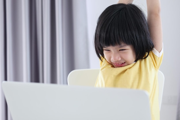Una pequeña estudiante asiática estudia en línea usando una computadora portátil en casa