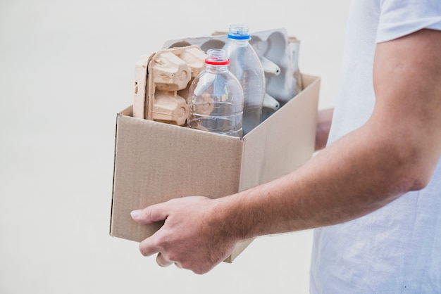 Foto el primer de la mano que sostiene recicla la caja con el cartón del huevo y las botellas plásticas en el contexto blanco