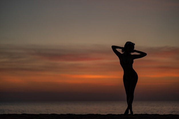 Foto retrato da silhueta de uma mulher de biquíni na praia, momento dourado do pôr do sol