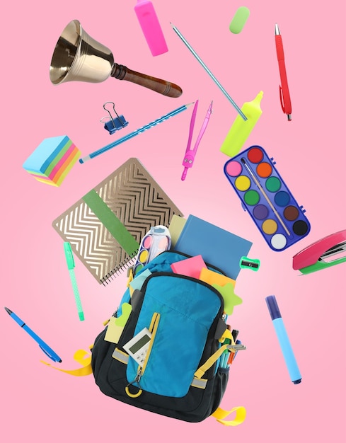 Foto sino da escola de mochila e diferentes artigos de papelaria voando no fundo rosa