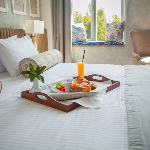 Foto gratuita croissant, huevo cocido, jugo de naranja, yogurt desayuno en bandeja en la cama en la habitación del hotel