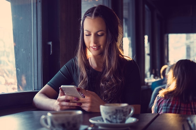 Atractiva mujer morena enviando mensajes de texto a un SMS en un café.