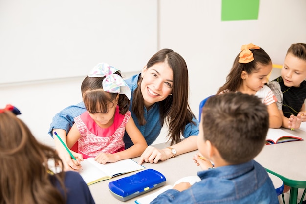 Foto gratuita buena maestra de preescolar hispana que disfruta de su trabajo y enseña a los estudiantes en un salón de clases