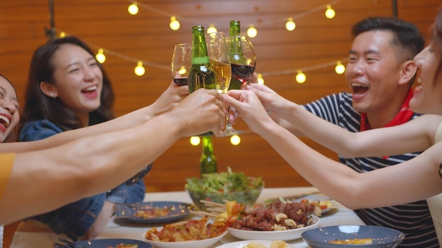 Foto gratuita grupo de personas asiáticas bebiendo alcohol animando una botella de cerveza y comiendo comida sentada en la mesa