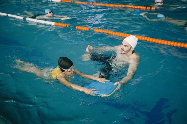 Foto gratuita entrenador enseñando a un niño en la piscina cubierta a nadar y bucear. lección de natación, desarrollo infantil.