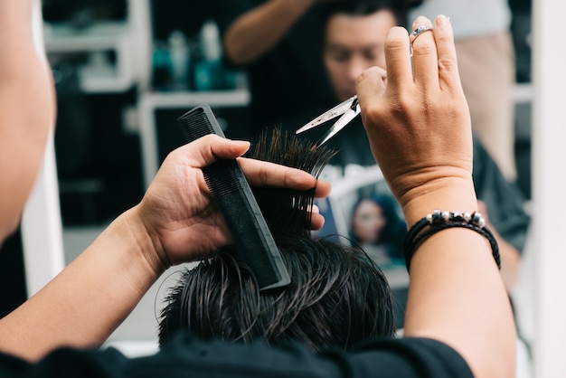 Foto gratuita estilista masculino irreconocible que corta el cabello del cliente frente al espejo