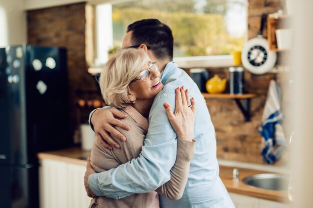 Foto gratuita feliz mujer madura y su hijo adulto abrazándose en la cocina