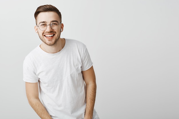 Foto gratuita hombre guapo con dientes blancos, sonriendo y con gafas sobre pared gris